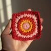Hand holding a colorful crochet granny square with detailed stitching.